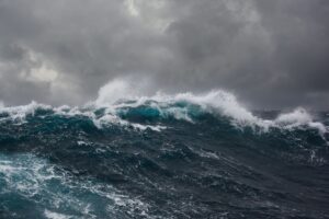 Large ocean waves crash under dark, stormy clouds, creating a dramatic and intense seascape.